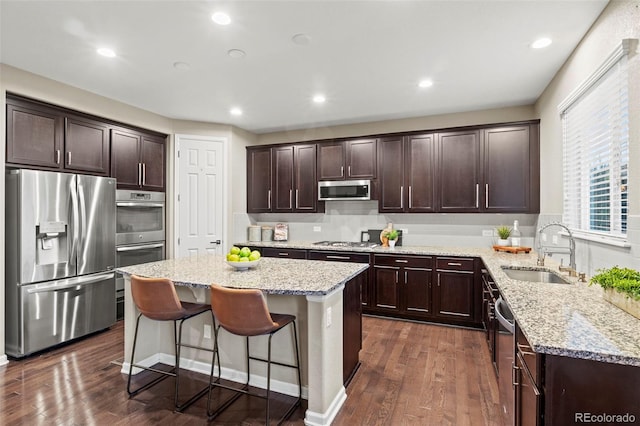 kitchen featuring sink, appliances with stainless steel finishes, a center island, light stone countertops, and dark hardwood / wood-style flooring