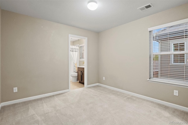 unfurnished bedroom featuring light carpet and ensuite bathroom