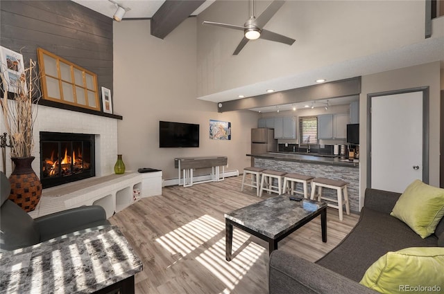 living room featuring track lighting, a baseboard heating unit, a fireplace, and light hardwood / wood-style floors