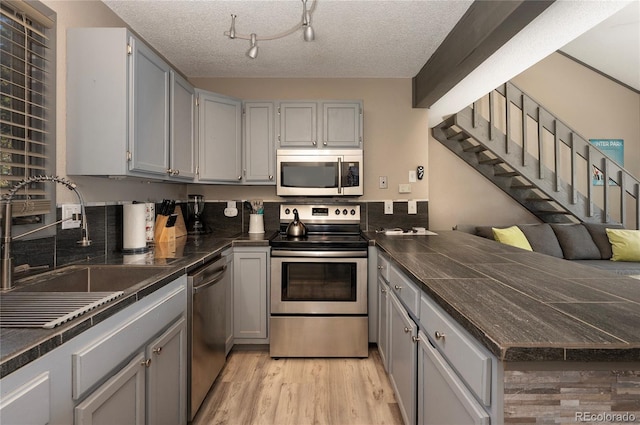 kitchen featuring a textured ceiling, light hardwood / wood-style flooring, stainless steel appliances, gray cabinets, and track lighting