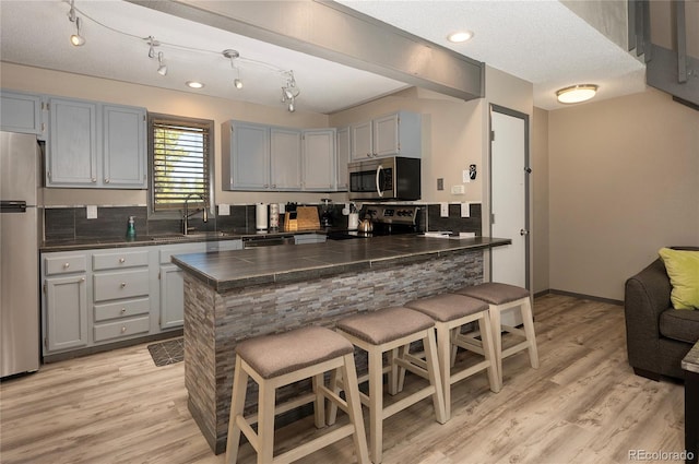 kitchen with a breakfast bar area, backsplash, appliances with stainless steel finishes, rail lighting, and light wood-type flooring