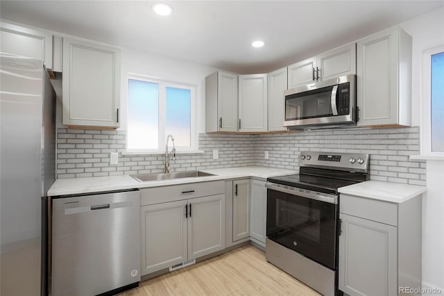 kitchen with tasteful backsplash, gray cabinetry, stainless steel appliances, sink, and light hardwood / wood-style floors