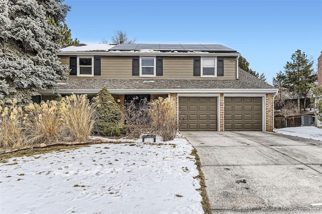 traditional-style home with a shingled roof, roof mounted solar panels, brick siding, and driveway