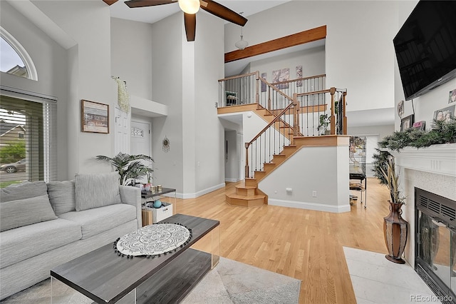 living room featuring a high ceiling, a tile fireplace, ceiling fan, and light hardwood / wood-style flooring