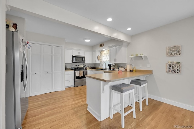 kitchen featuring appliances with stainless steel finishes, white cabinetry, a kitchen breakfast bar, light hardwood / wood-style floors, and kitchen peninsula