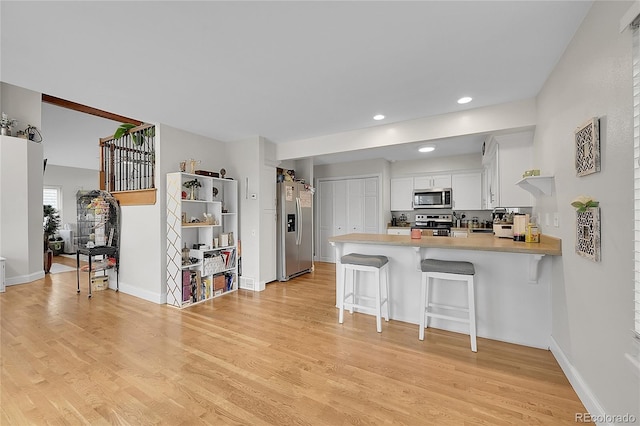 kitchen with appliances with stainless steel finishes, white cabinetry, a breakfast bar area, kitchen peninsula, and light wood-type flooring