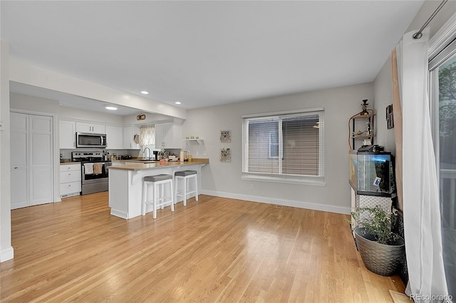 kitchen with a breakfast bar area, stainless steel appliances, white cabinets, kitchen peninsula, and light wood-type flooring