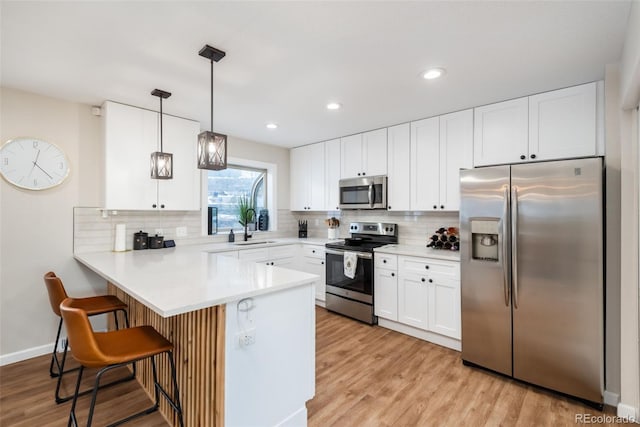 kitchen with kitchen peninsula, a kitchen breakfast bar, appliances with stainless steel finishes, backsplash, and white cabinetry