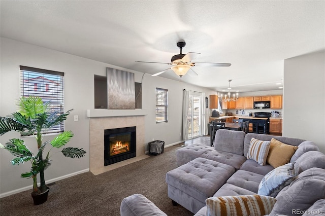 carpeted living room featuring a tiled fireplace, ceiling fan with notable chandelier, and a textured ceiling