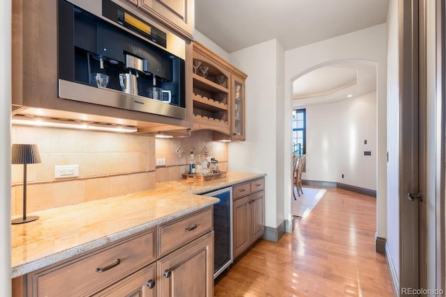5810 Amber Ridge Dr, Castle Pines, CO 80108 - indoor dry bar featuring arched walkways, beverage cooler, decorative backsplash, light wood-style flooring, and baseboards