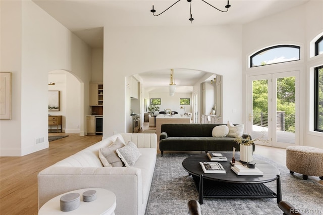 8937 Little Raven Trl, Niwot, CO 80503 - living room featuring arched walkways, a towering ceiling, a chandelier, and light wood-style floors