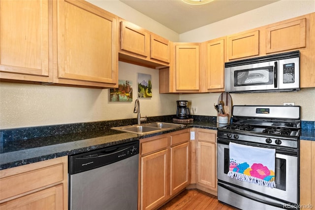 kitchen with appliances with stainless steel finishes, light hardwood / wood-style floors, dark stone countertops, and sink