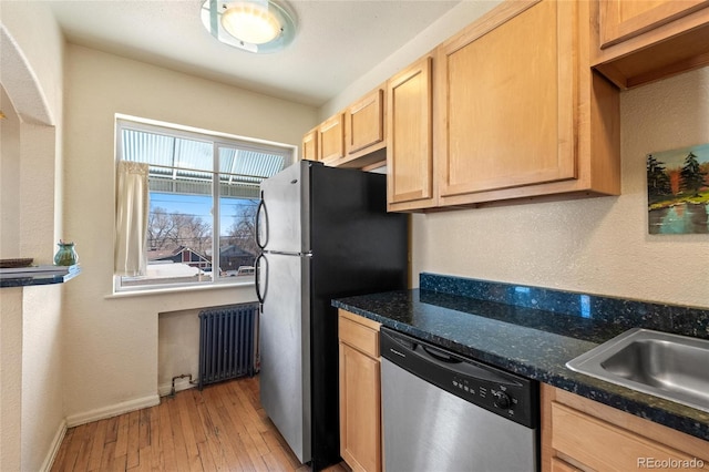 kitchen featuring appliances with stainless steel finishes, light hardwood / wood-style floors, dark stone countertops, light brown cabinets, and radiator