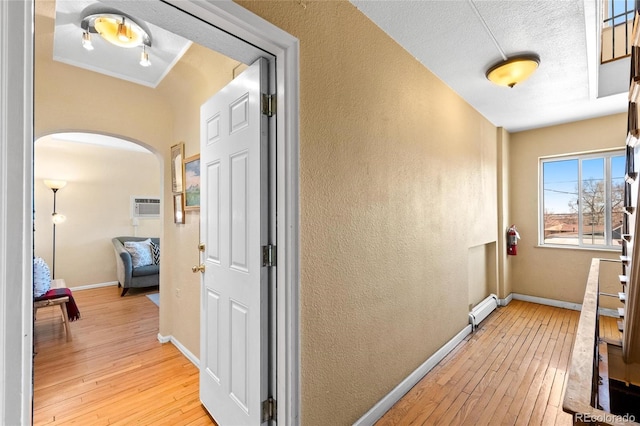 corridor with a wall mounted AC, light hardwood / wood-style floors, baseboard heating, and a textured ceiling