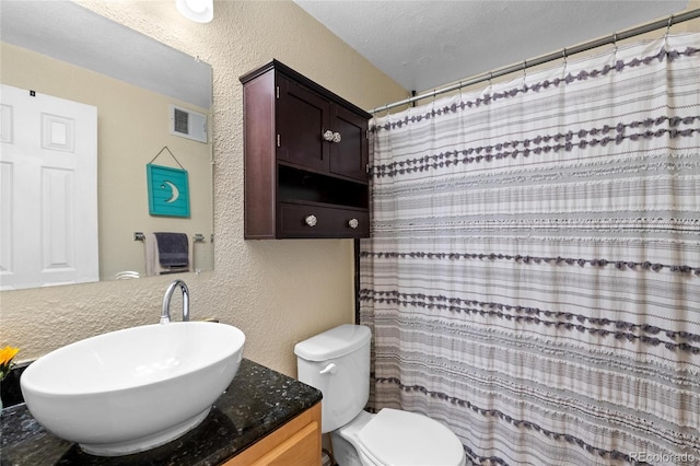 bathroom with a textured ceiling, walk in shower, vanity, and toilet