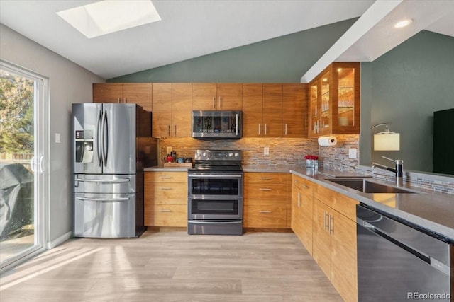 kitchen featuring vaulted ceiling with skylight, decorative backsplash, glass insert cabinets, stainless steel appliances, and a sink