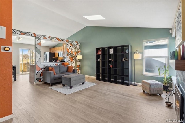 living area with baseboards, lofted ceiling with skylight, and light wood-style floors