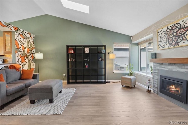 living area featuring light wood finished floors, lofted ceiling with skylight, a glass covered fireplace, and baseboards