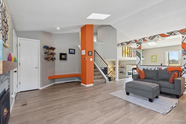 living area featuring lofted ceiling with skylight, light wood-style flooring, stairway, and baseboards