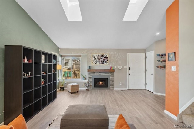 living room with a warm lit fireplace, vaulted ceiling with skylight, wood finished floors, and baseboards