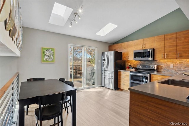 kitchen featuring vaulted ceiling with skylight, stainless steel appliances, a sink, light wood-style floors, and backsplash