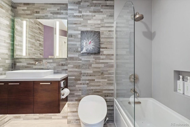 full bath featuring toilet, combined bath / shower with glass door, tile walls, and vanity