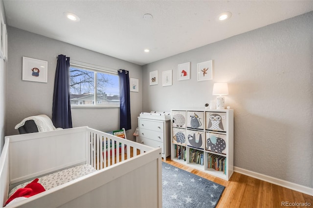 bedroom featuring light wood-type flooring, a crib, baseboards, and recessed lighting