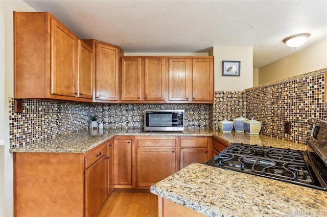 11855 Humboldt Dr, Northglenn, CO 80233 - kitchen with stainless steel microwave, black range with gas stovetop, light wood-style flooring, light stone counters, and backsplash
