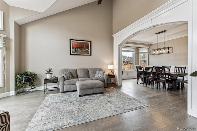 living area featuring baseboards, arched walkways, wood finished floors, crown molding, and a notable chandelier