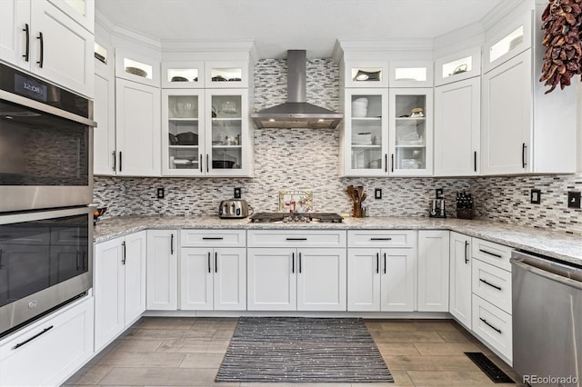 kitchen featuring white cabinets, wall chimney range hood, stainless steel appliances, and backsplash