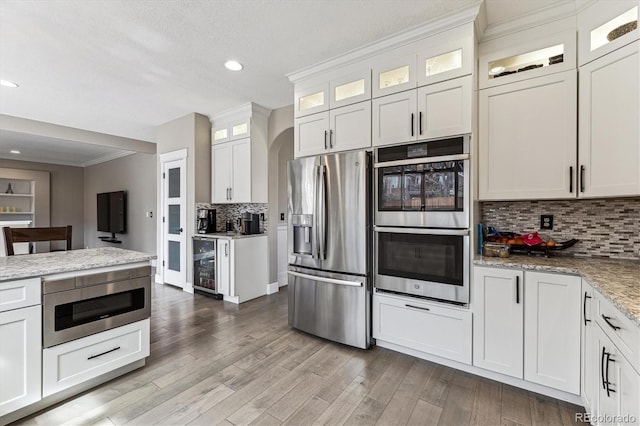 kitchen with ornamental molding, stainless steel appliances, wine cooler, and light wood-style floors