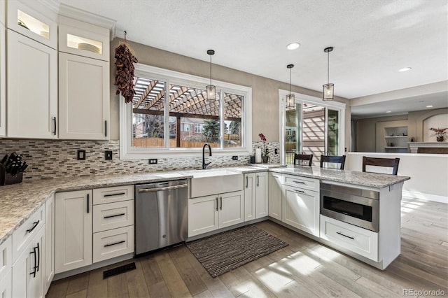 kitchen with appliances with stainless steel finishes, light wood-style flooring, a peninsula, and decorative backsplash