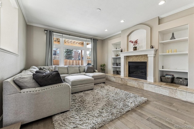 living area with built in shelves, a fireplace, crown molding, and wood finished floors