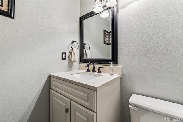 bathroom featuring toilet, vanity, and a textured wall