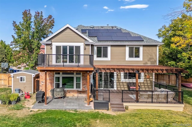 rear view of house with a balcony, solar panels, an outdoor structure, a lawn, and a patio area