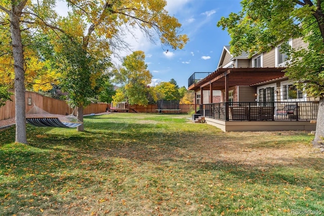 view of yard featuring a trampoline, a fenced backyard, and a deck