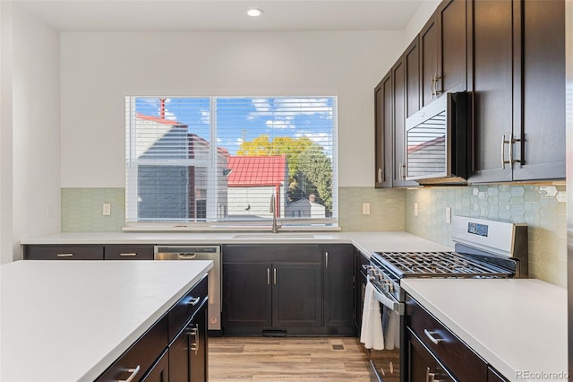 kitchen featuring stainless steel appliances, light countertops, a sink, dark brown cabinetry, and light wood-type flooring