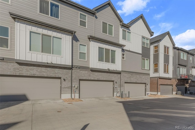 multi unit property with central air condition unit, a garage, brick siding, a residential view, and board and batten siding