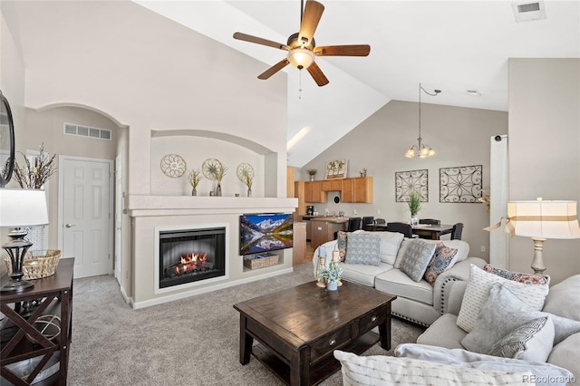 living area featuring high vaulted ceiling, visible vents, ceiling fan with notable chandelier, and light carpet