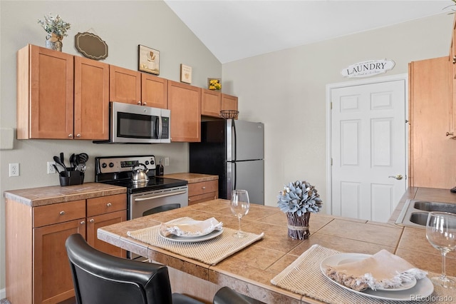 kitchen featuring brown cabinetry, a breakfast bar, vaulted ceiling, light countertops, and appliances with stainless steel finishes