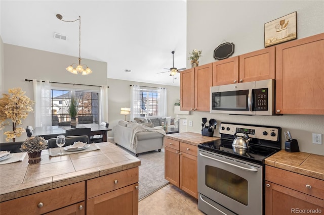 kitchen with ceiling fan with notable chandelier, visible vents, pendant lighting, tile counters, and appliances with stainless steel finishes