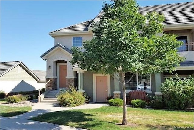 view of front of house with stone siding, stucco siding, a tiled roof, and a front yard