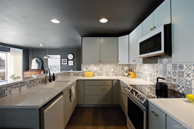 kitchen with appliances with stainless steel finishes, sink, dark hardwood / wood-style floors, kitchen peninsula, and gray cabinetry