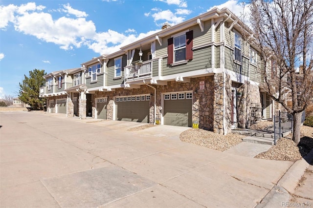 townhome / multi-family property with a balcony, a garage, a residential view, stone siding, and driveway