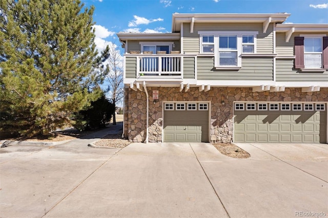 view of property featuring a balcony, stone siding, an attached garage, and concrete driveway