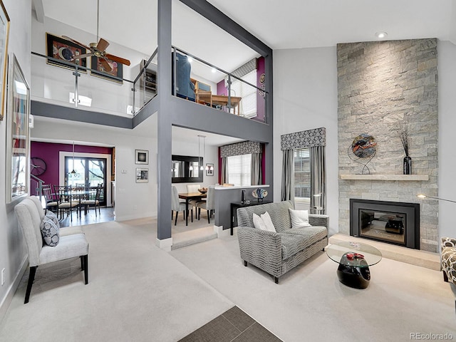 living area featuring baseboards, a stone fireplace, a healthy amount of sunlight, and carpet