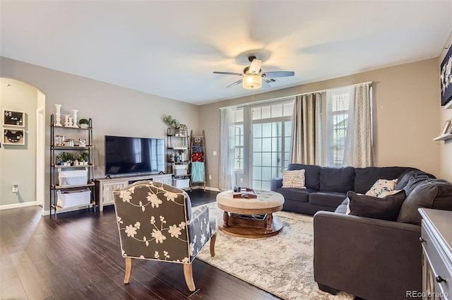 living room featuring baseboards, arched walkways, dark wood finished floors, and ceiling fan