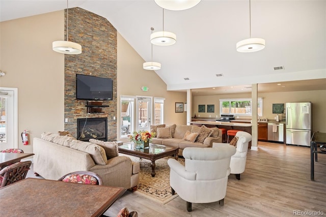 living room featuring a fireplace, high vaulted ceiling, light hardwood / wood-style flooring, and a healthy amount of sunlight