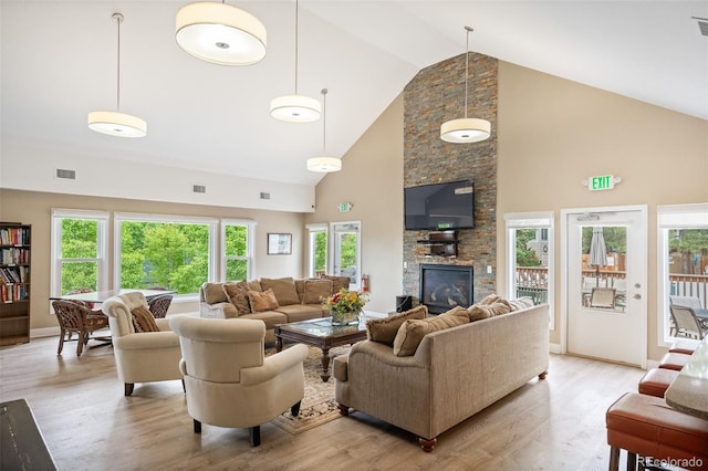 living room with high vaulted ceiling, light wood-type flooring, and a stone fireplace