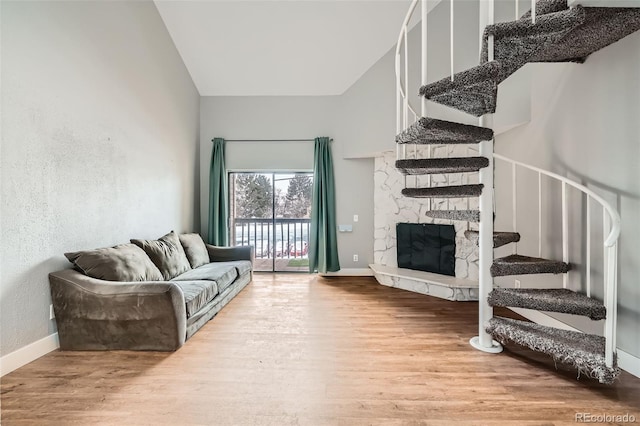 living room featuring a stone fireplace, wood-type flooring, and a high ceiling